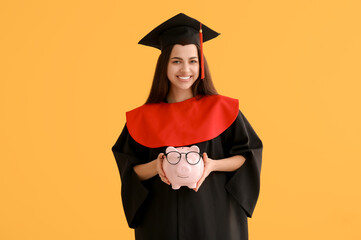 Happy female graduate with piggy bank on yellow background. Tuition fees concept
