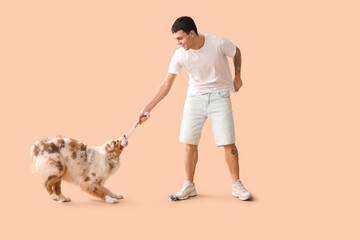 Young man playing with Australian Shepherd dog on beige background
