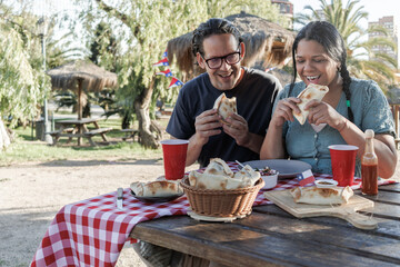 A couple shares an intimate outdoor meal in the park. Both are happy and laughing, about to bite...