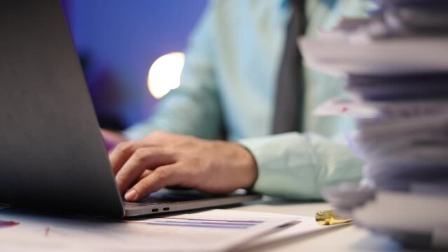 Man working with laptop and stack of documents on desk. Working to meet the deadline.