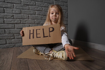 Homeless little girl begging for help near grey brick wall