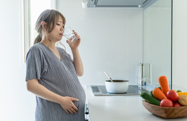キッチンで水を飲む妊娠後期の妊婦の女性（水分補給・悪阻）
