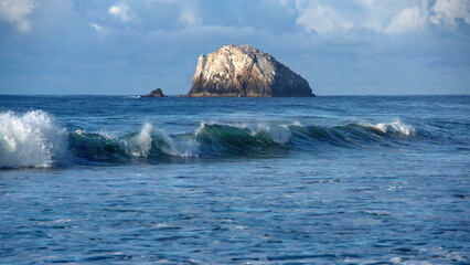 Waves breaking on the beach, with a rocky islet in the background, in Zipolite, Mexico