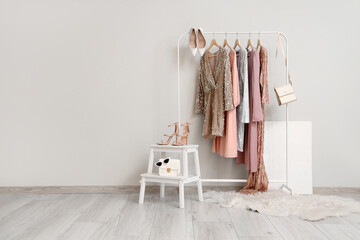 Rack of stylish dresses and trendy heels near white wall