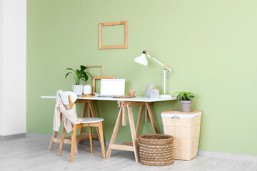 Stylish workplace with lamp, houseplants and laptop in light office