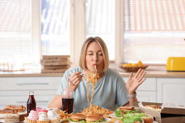 Beautiful woman with tasty pasta at table in kitchen. Overeating concept