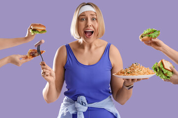 Shocked sporty woman and hands with unhealthy food on lilac background. Overeating concept