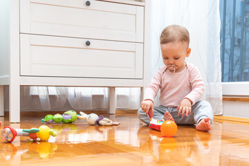 A baby with a pacifier in his mouth interacts with interest with toys while playing in the room