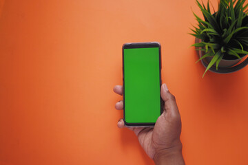 top view of young man hand using smart phone with green screen on orange color background 