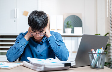 depressed, despair, unhappy, executive, sad, frustration, loss, manager, overwhelmed, job. A man is sitting at a desk with a laptop and a stack of papers. and he is in a state of distress.