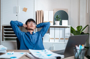 executive, job, manager, exhausted, rest, occupation, overworked, paperwork, break, hardworking. A man is sitting at a desk with a laptop and a potted plant. He is relaxed and focused on his work.