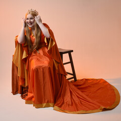 Full length portrait of plus size blonde woman, wearing historical medieval fantasy gown, golden crown  royal queen. sitting pose on throne chair, isolated studio background.