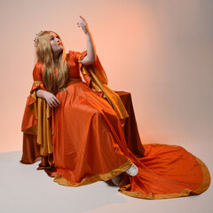 Full length portrait of plus size blonde woman, wearing historical medieval fantasy gown, golden crown  royal queen. sitting pose on throne chair, isolated studio background.