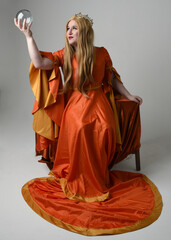 Full length portrait of plus size blonde woman, wearing historical medieval fantasy gown, golden crown  royal queen. sitting pose on throne chair, isolated studio background.