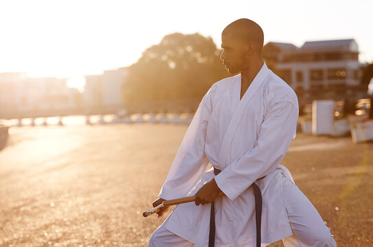 Serious man, karate and fitness with nunchuck in city for kata, fighting technique or style. Young male person or muay thai fighter with weapon for martial arts or self defense on street in town