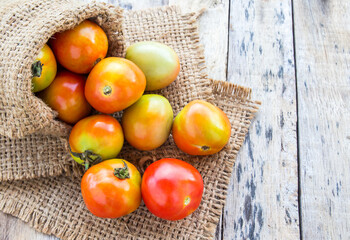 Fresh tomatoes in burlap sack on wooden table