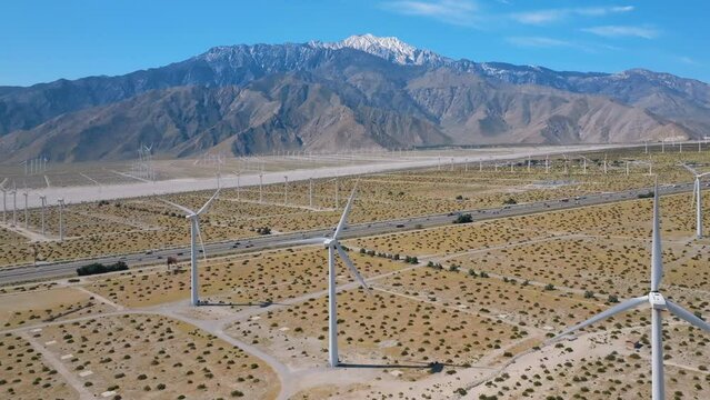 Establishing shot of interstate 10 freeway near Palm Springs surrounded by wind turbines and snow capped mountains in the distance