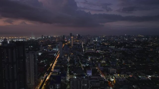 Aerial ascending footage of metropolis in evening. High rise buildings and streets in urban borough. Manila, Philippines