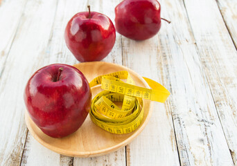 Red apple and yellow tape measure on a wooden table
