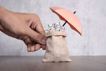 Hand holding umbrella protecting bag of money. Financial safety, income protection insurance...