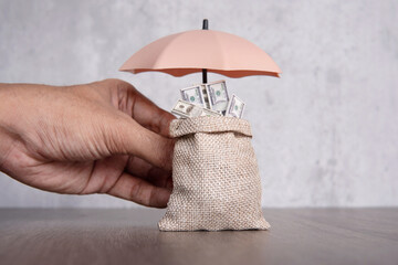 Hand holding umbrella protecting bag of money. Financial safety, income protection insurance...