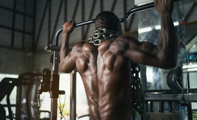 A man is lifting weights in a gym. He is wearing a chain around his neck. The chain is attached to...