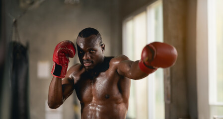 A man in a boxing ring with sweat on his face. He is wearing a red glove. Scene is intense and focused