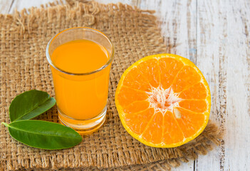 Glass of freshly pressed orange juice with sliced orange on wooden table