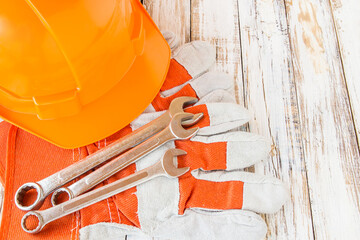 Leather work gloves and safety hat with wrench on wooden table