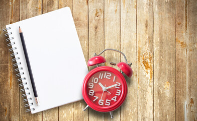 Red alarm clock and note book on brown wooden