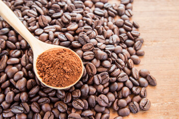 Coffee powder in wooden spoon and coffee beans on wooden table