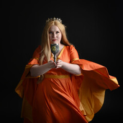 close up portrait of plus sized blonde woman, wearing historical medieval fantasy gown, crowned royal queen.  posing holding wine cup drinking goblet, isolated dark black studio background.

