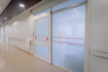 a bright hospital corridor with numbered doors, frosted glass windows, handrails, and a paper towel...