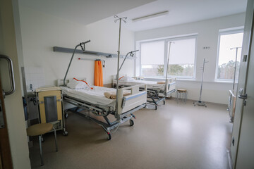 Fototapeta na wymiar Valmiera, Latvia - March 20, 2024 - A hospital room with two empty beds, IV stands, a chair, large windows with a view, and various medical equipment.