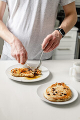 man cutting into homemade pancakes with maple syrup