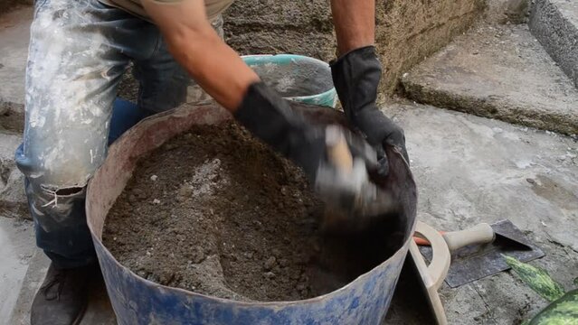 Senior caucasian bricklayer mixing cement and sand in container.