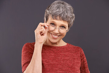 Happy, portrait and senior woman with glasses in studio for vision, optometry or frame sale on grey...