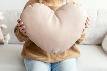Woman sitting on couch holding a heart sharped pillow