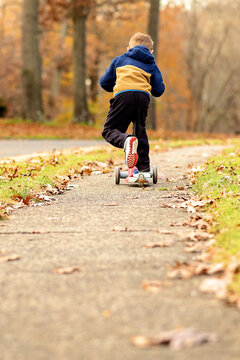 Young Boy Riding Scooter on Sidewalk in the Fall