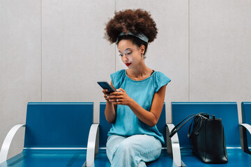 Focused young ethnic woman sitting and browsing smartphone