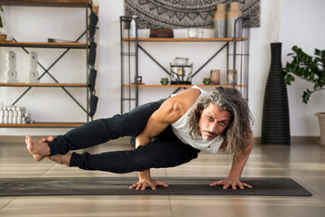 Flexible man doing Astavakrasana on mat at home