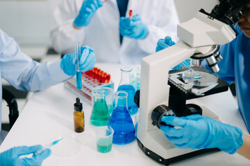 Fototapeta premium Team scientists conducting research investigations in a medical laboratory, a researcher in the foreground is using a microscope in laboratory