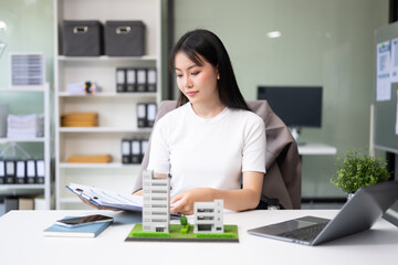 Young real estate agent worker working with laptop and tablet at table in office and small house beside it..