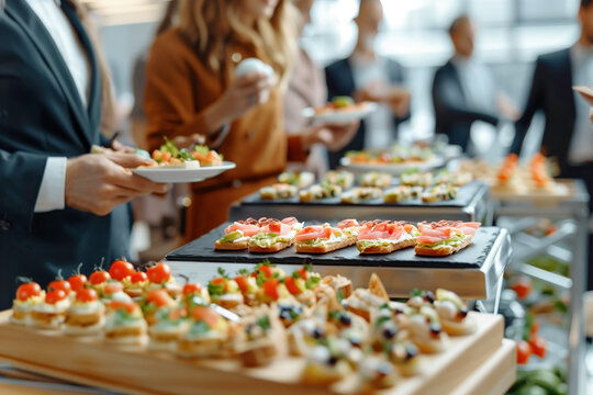 Business people serving themselves by picking up canapes served on table at brunch buffet indoors.