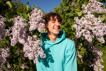 Portrait of a handsome young man on a background of lilac flowers. A student poses looking at the camera.