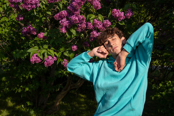 Portrait of a handsome young man on a background of lilac flowers. A student poses looking at the camera.