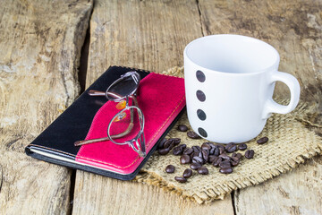 Glasses, notebook, coffee mugs and coffee beans on wooden table