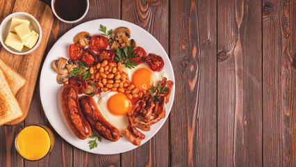 Traditional full English breakfast with fried eggs, sausages, beans, mushrooms, grilled tomatoes and bacon on wooden background.