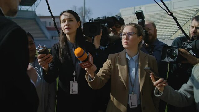 Interview of football team director at press conference for TV news. Organization representative answering questions and giving interview outside a soccer stadium. Journalists crowd on press campaign.