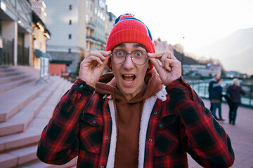 A young student on the background of a city street. Travel in the cold season. A man in a jacket and hat looks at the camera.